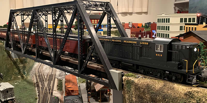 Photo of the layout with the PRSL-AS616 Locomotive pulling passenger cars across a girder bridge.